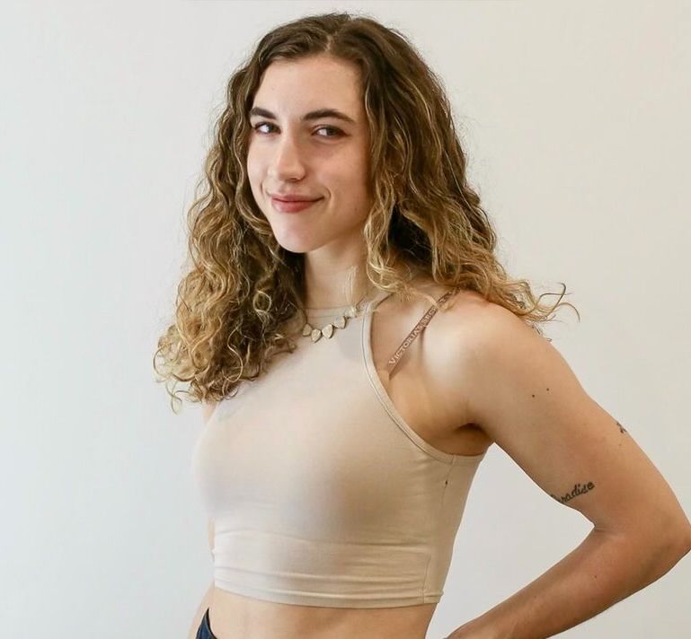 A woman with curly hair is wearing a tan crop top.