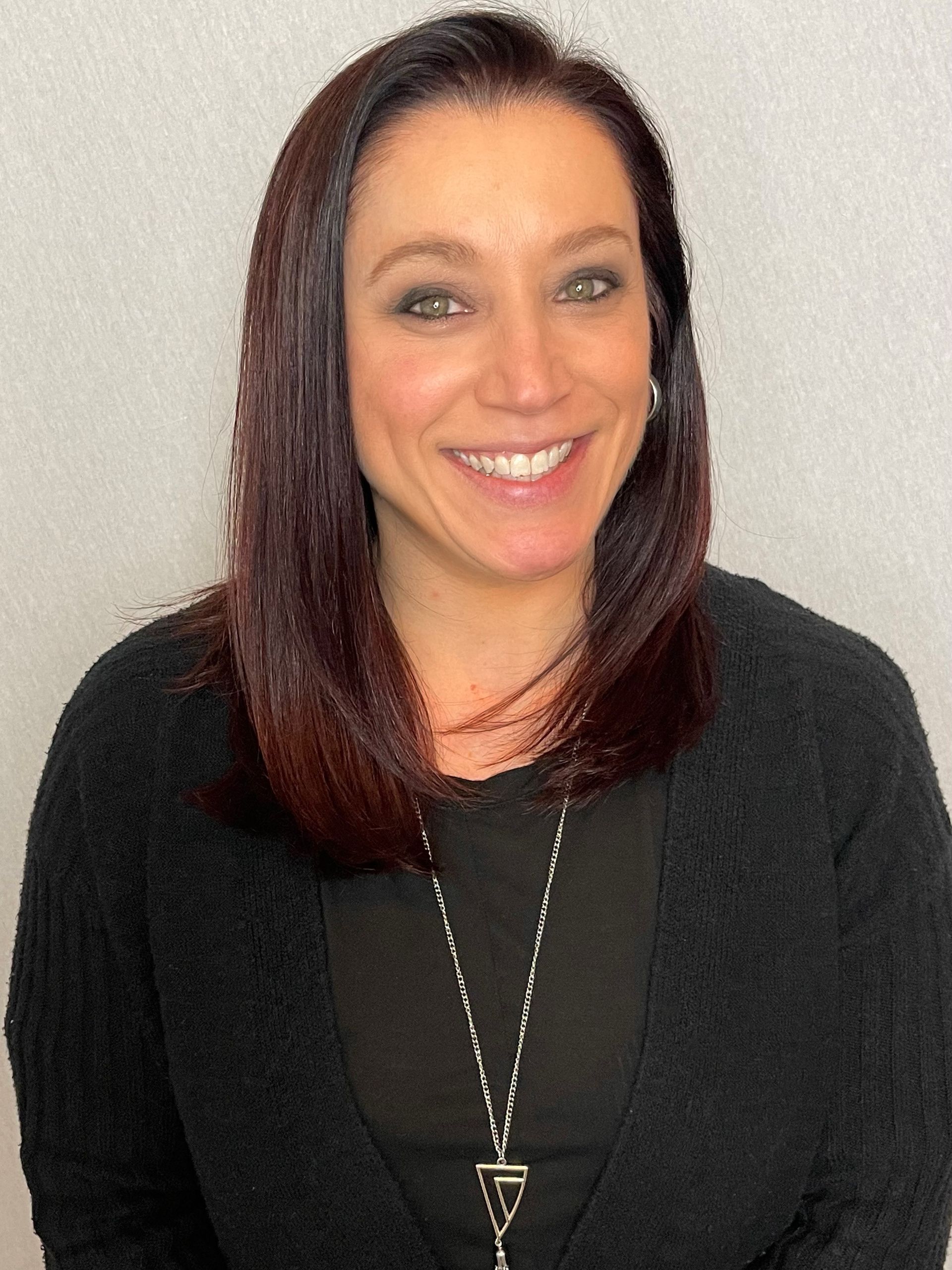 A woman wearing a black sweater and a necklace is smiling for the camera.