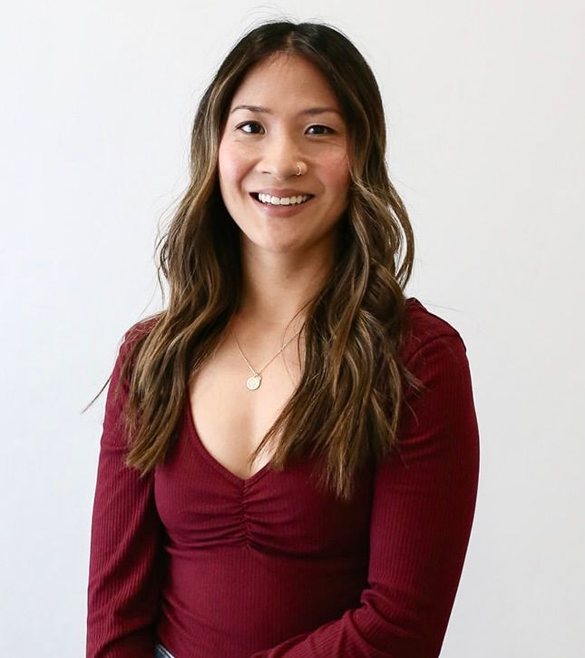 A woman wearing a red shirt and a necklace is smiling for the camera.