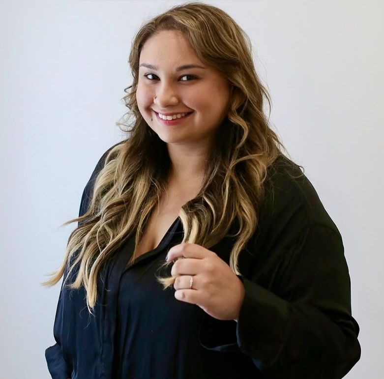 A woman in a black shirt is smiling and holding her hair