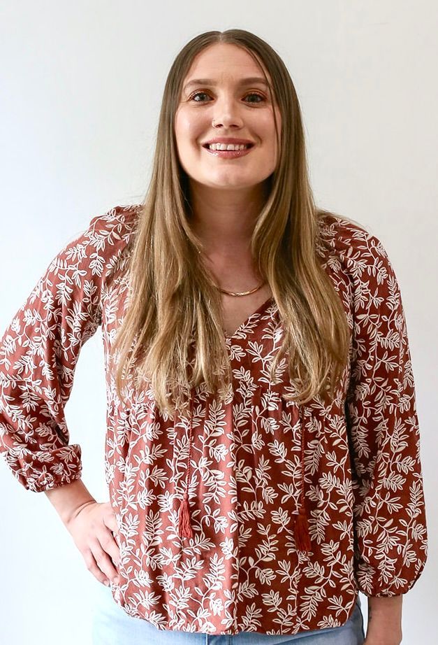 A woman wearing a red floral blouse is standing with her hands on her hips.