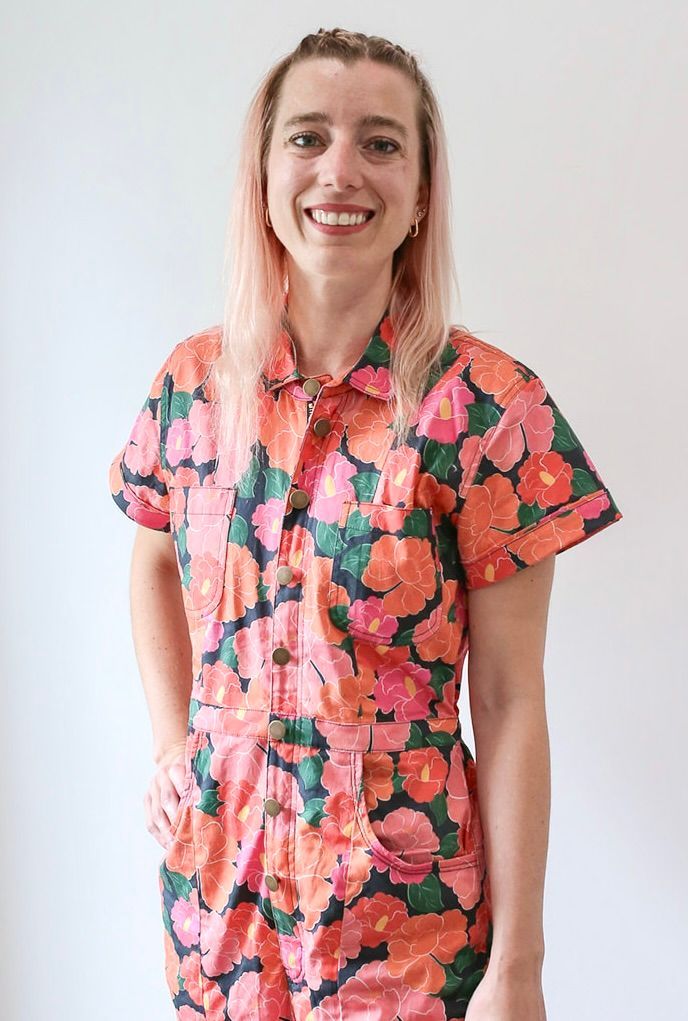 A woman is wearing a floral jumpsuit and smiling.