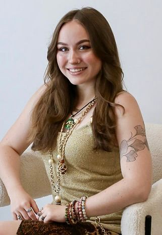 A woman in a gold dress is sitting in a chair and smiling.