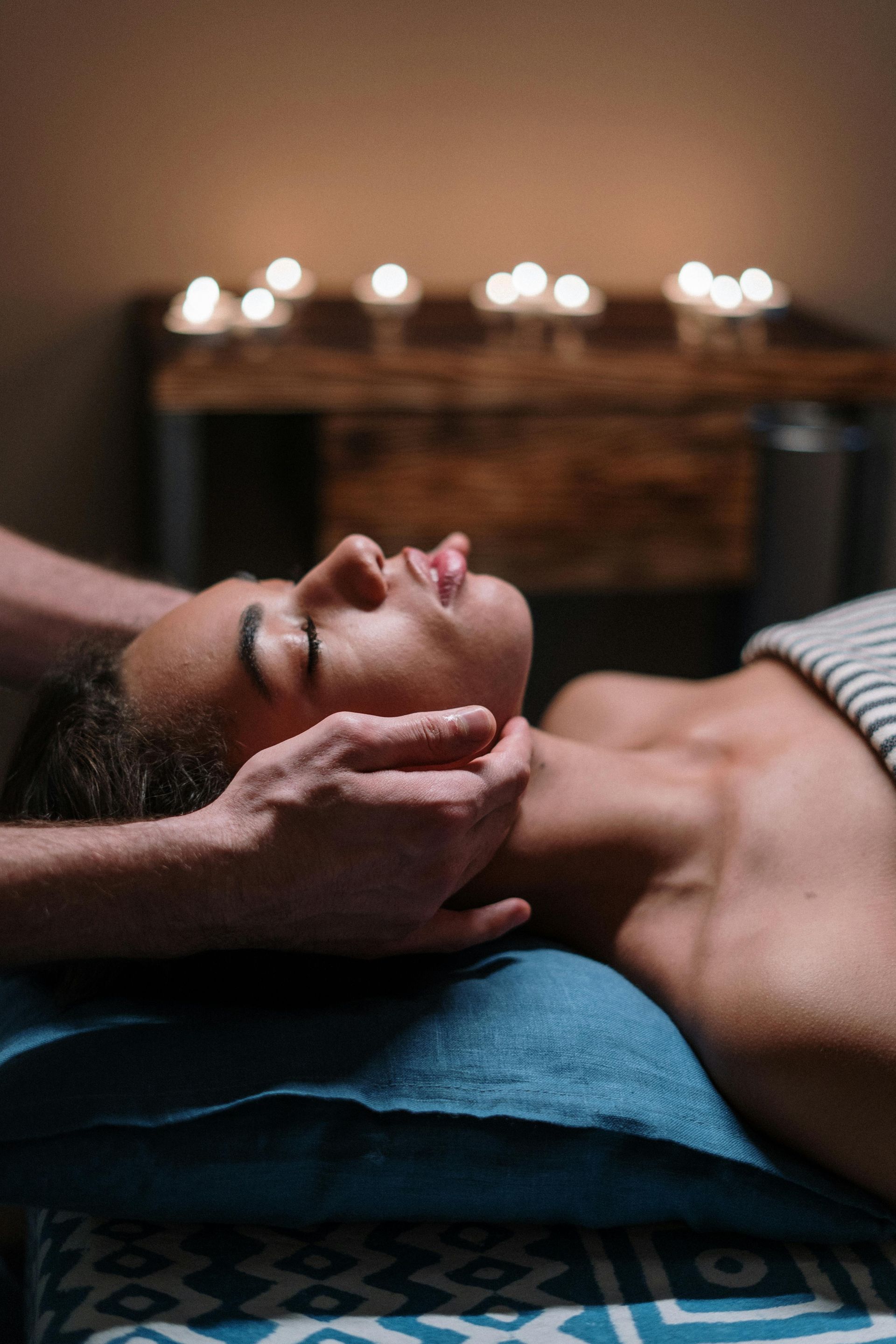 Person receiving a facial massage, relaxed with eyes closed; lit candles in background.