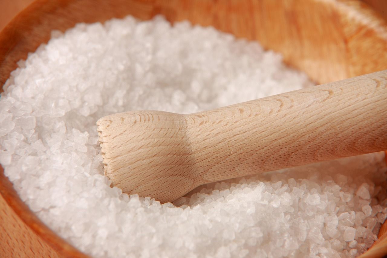 Wooden bowl filled with white salt, a wooden pestle partially submerged.