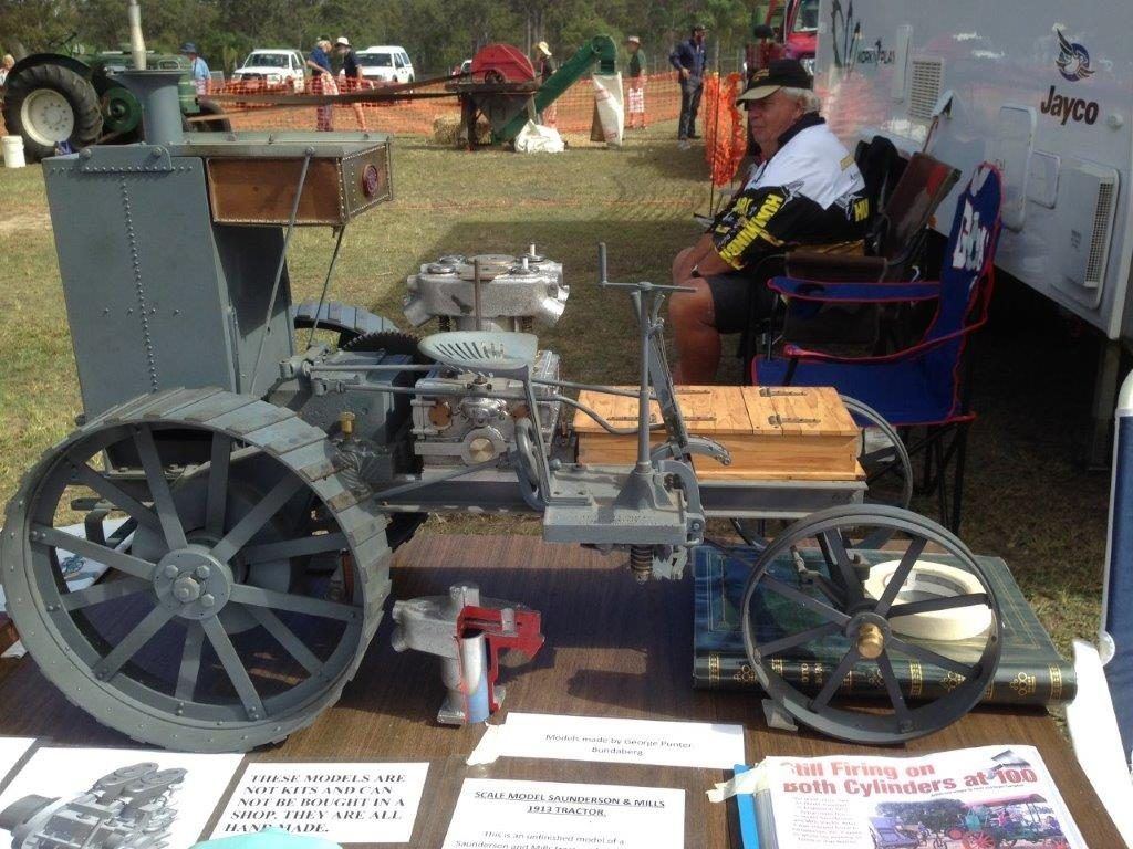 A man is sitting in a chair next to a model tractor on a table.