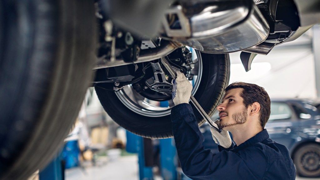 A man is working on the underside of a car in a garage | Karta Motorwerks