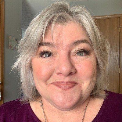 A woman with gray hair is smiling and wearing a purple shirt.