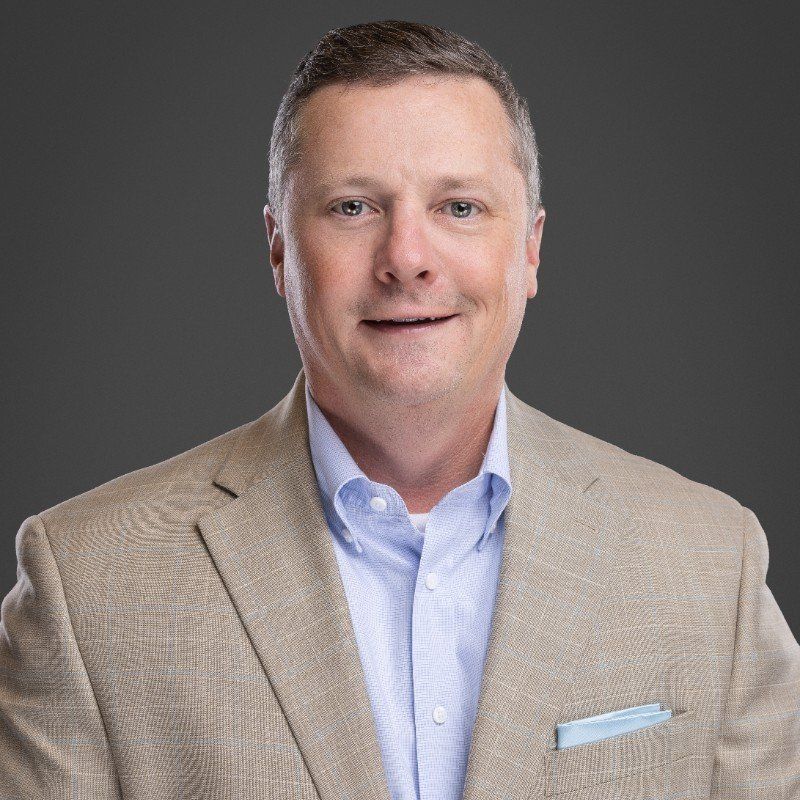 A man in a tan suit and blue shirt is smiling for the camera.