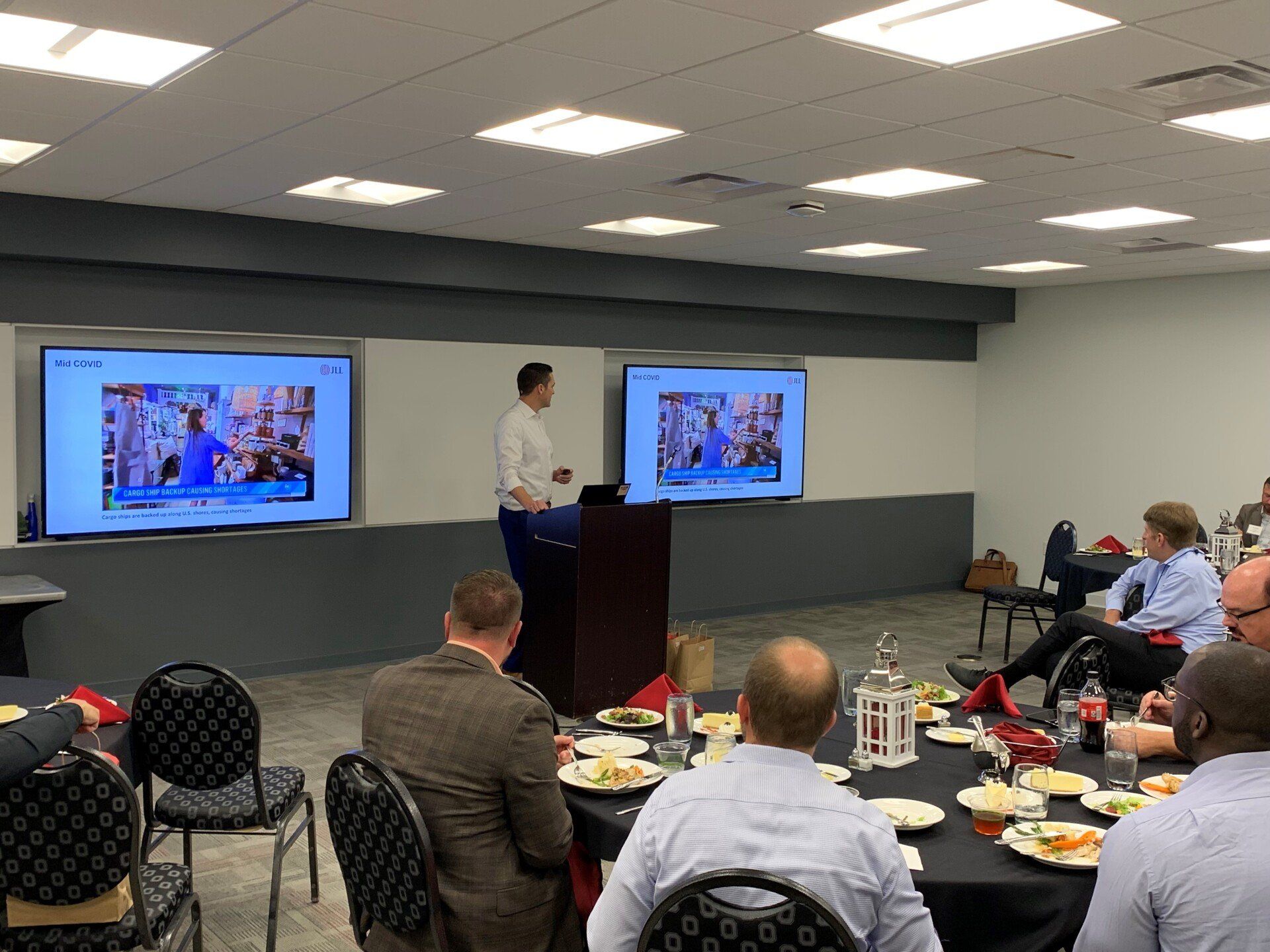 A man is giving a presentation to a group of people sitting at tables.