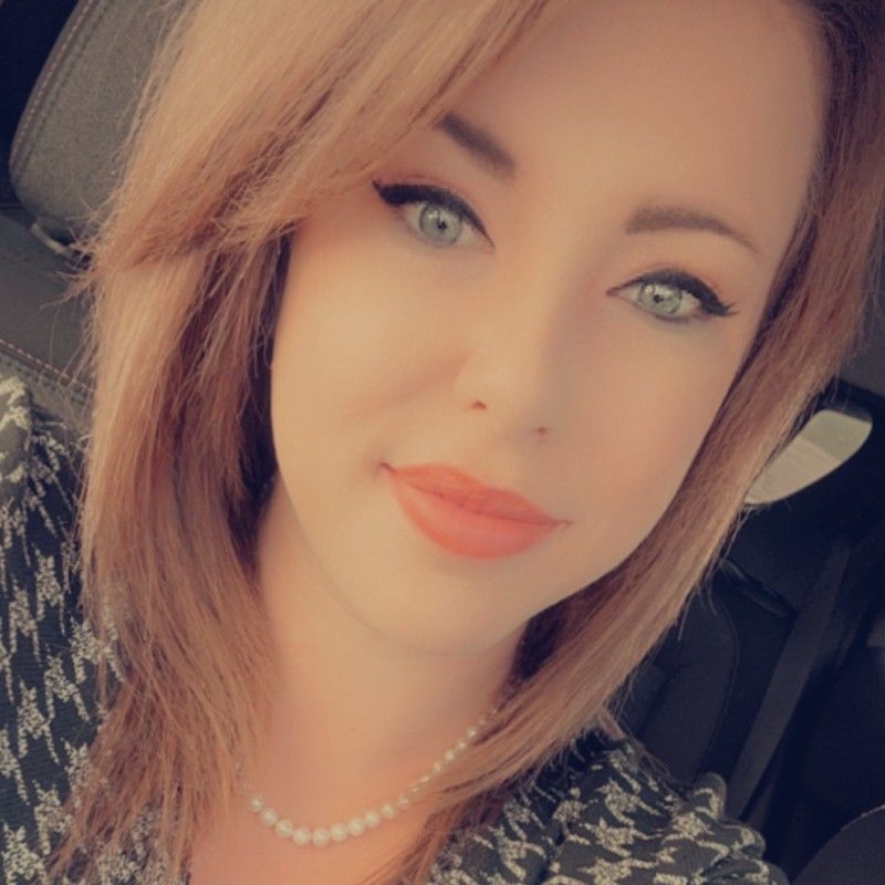 A woman wearing a pearl necklace is taking a selfie in a car.