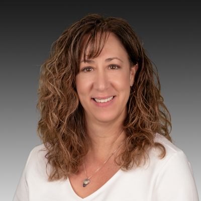 A woman wearing a black turtleneck and a necklace is smiling for the camera.