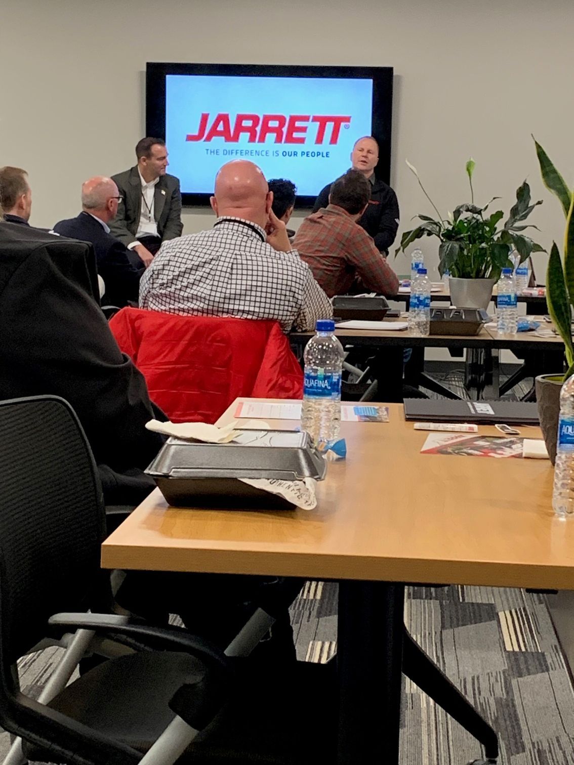 A group of people are sitting at tables in front of a screen that says jarrett