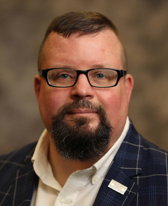 A man with a beard and glasses is wearing a suit.