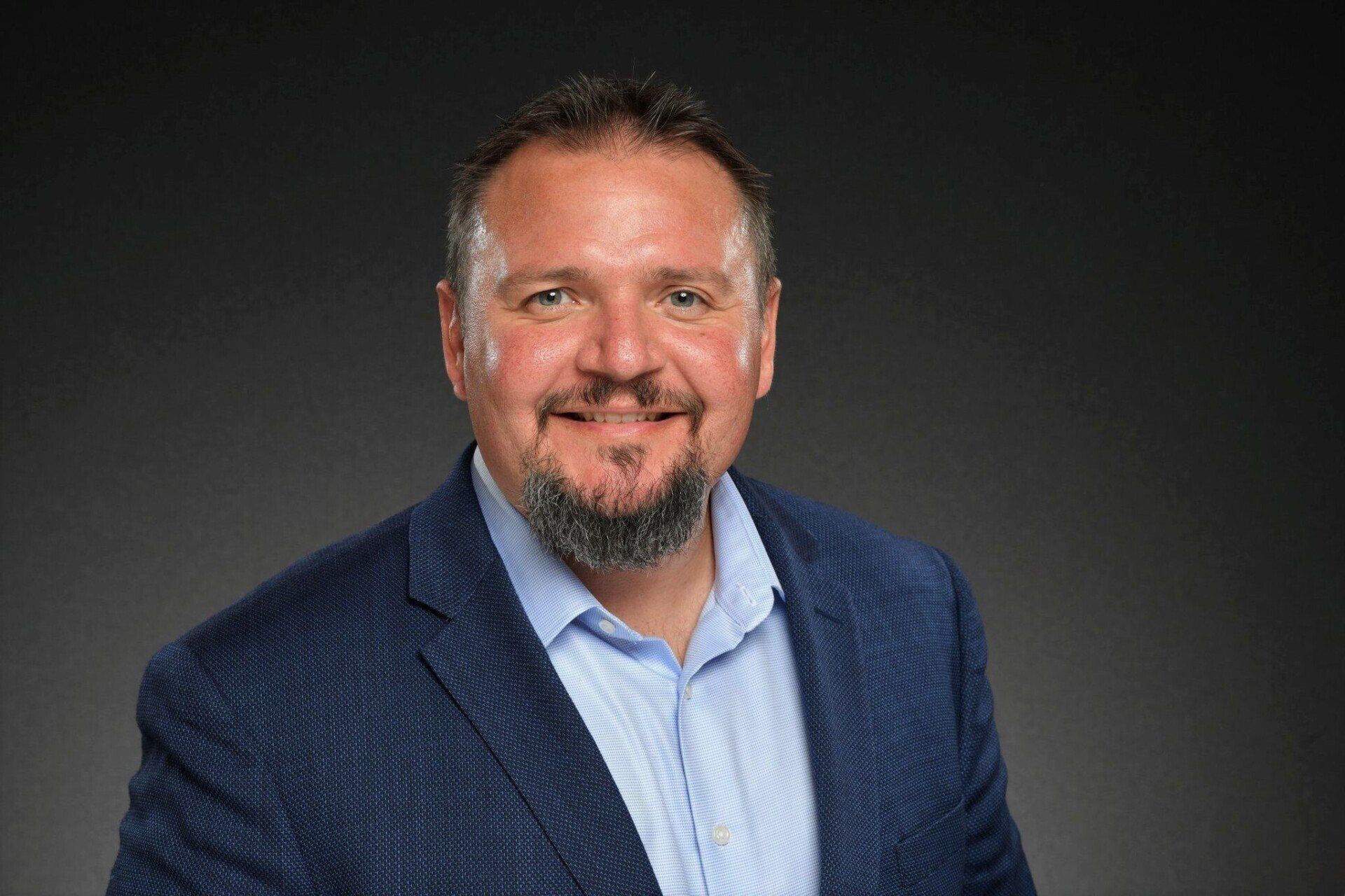 A man with a beard is wearing a suit and smiling for the camera.