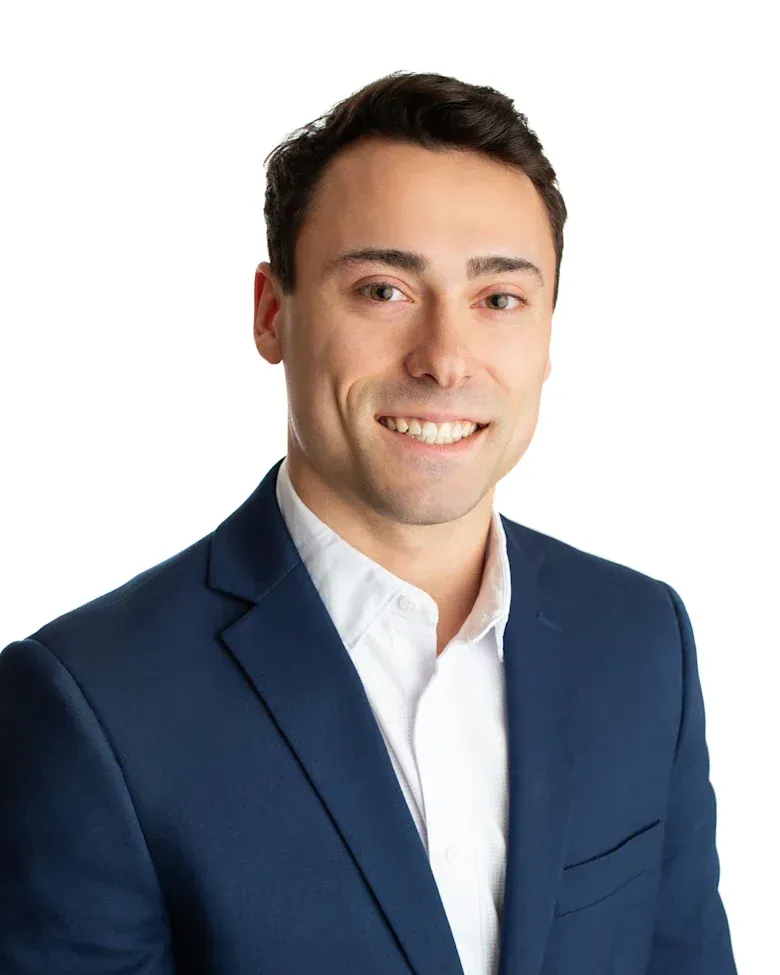 A man in a tan suit and blue shirt is smiling for the camera.