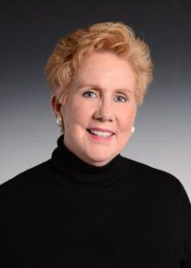 A woman wearing a black turtleneck and earrings is smiling for the camera.