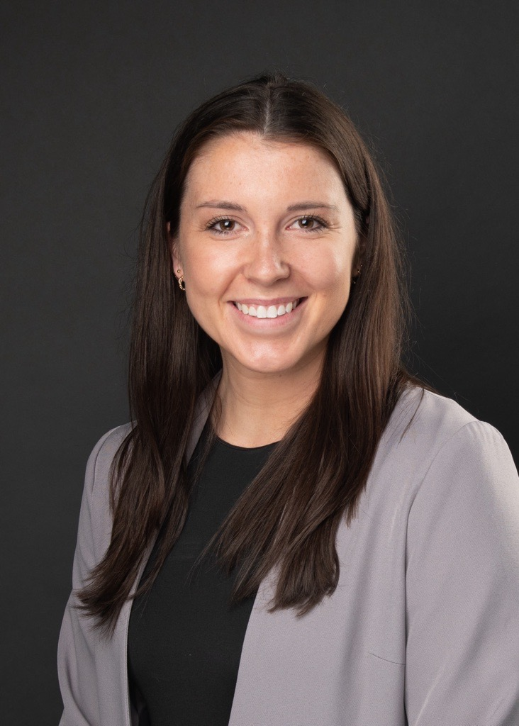 A woman wearing a gray jacket and a black shirt is smiling for the camera.
