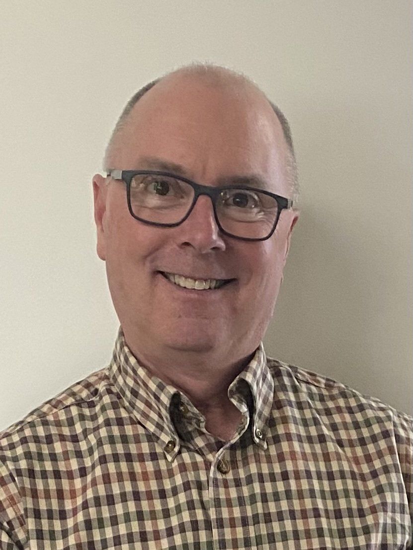 A man wearing glasses and a plaid shirt is smiling for the camera.