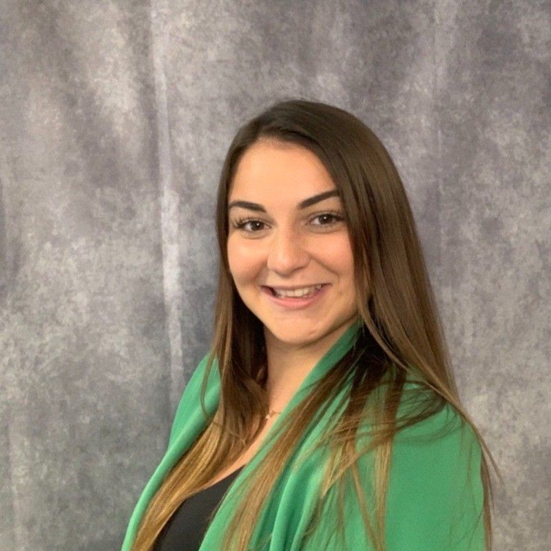 A woman wearing a green jacket and scarf is smiling for the camera.