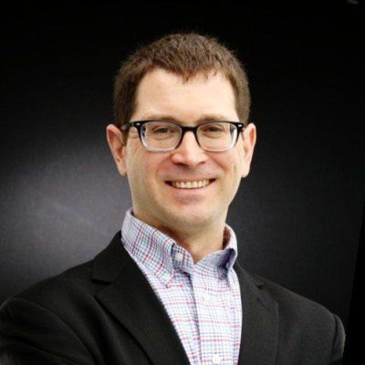 A man wearing glasses and a suit is smiling for the camera.