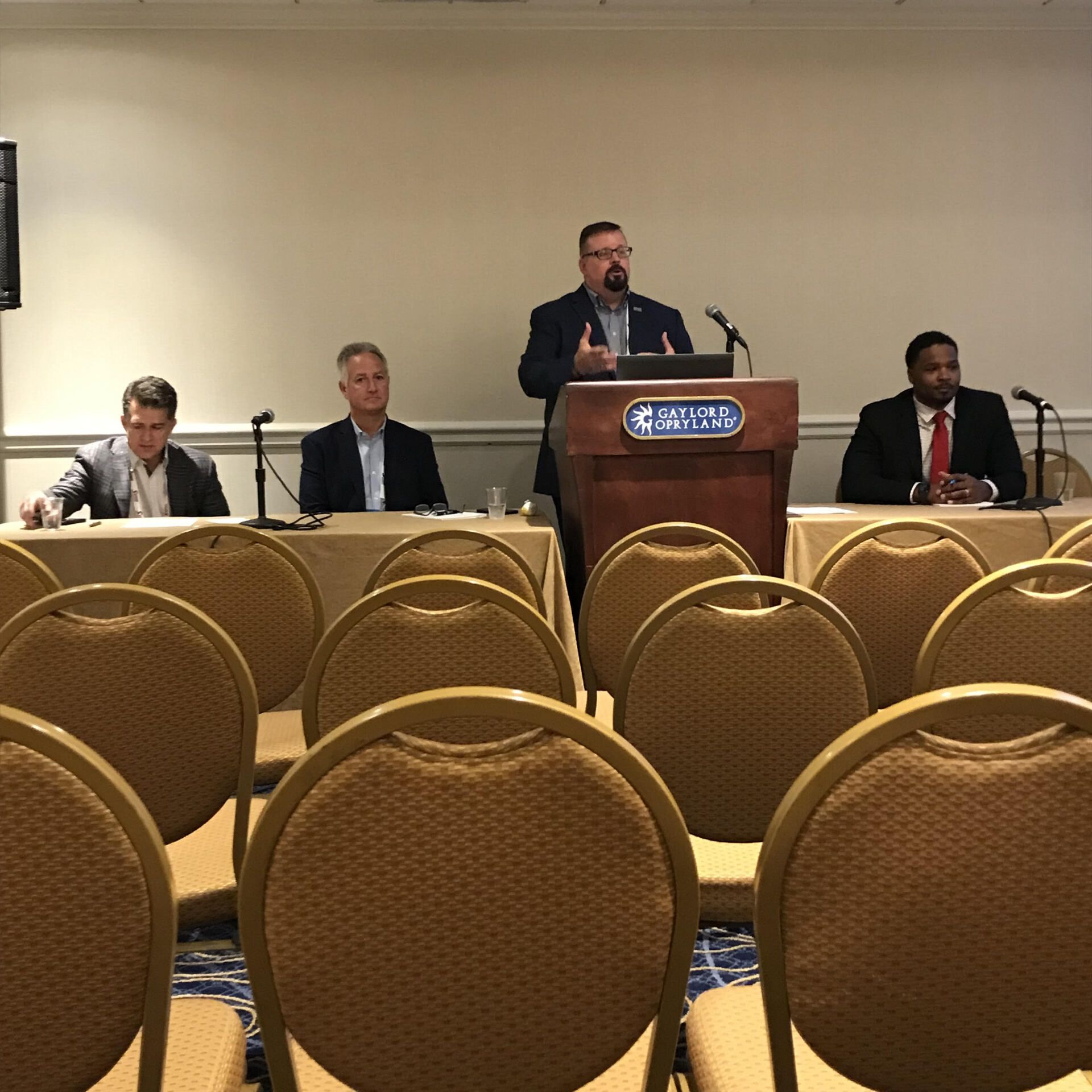 A man stands at a podium in front of a row of chairs