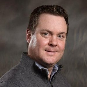 A man in a grey sweater is smiling for the camera.