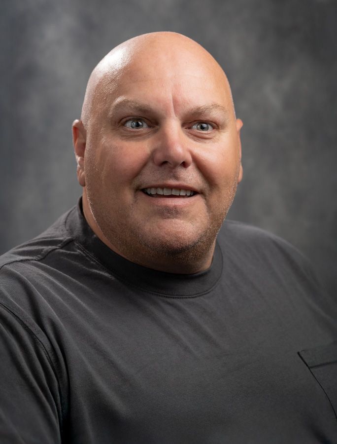 A bald man wearing a black shirt is smiling for the camera.