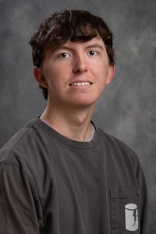 A young man is wearing a gray t-shirt with a lightning bolt on the pocket.