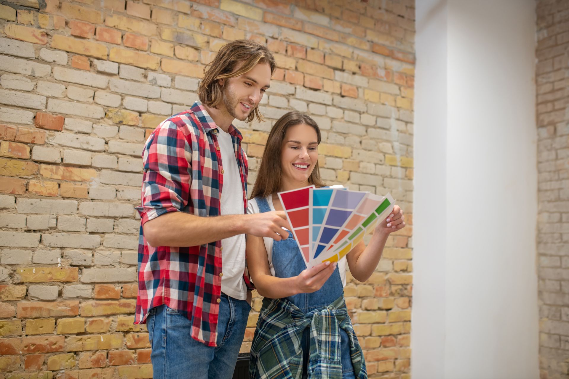 A man and a woman are looking at a color palette in front of a brick wall.