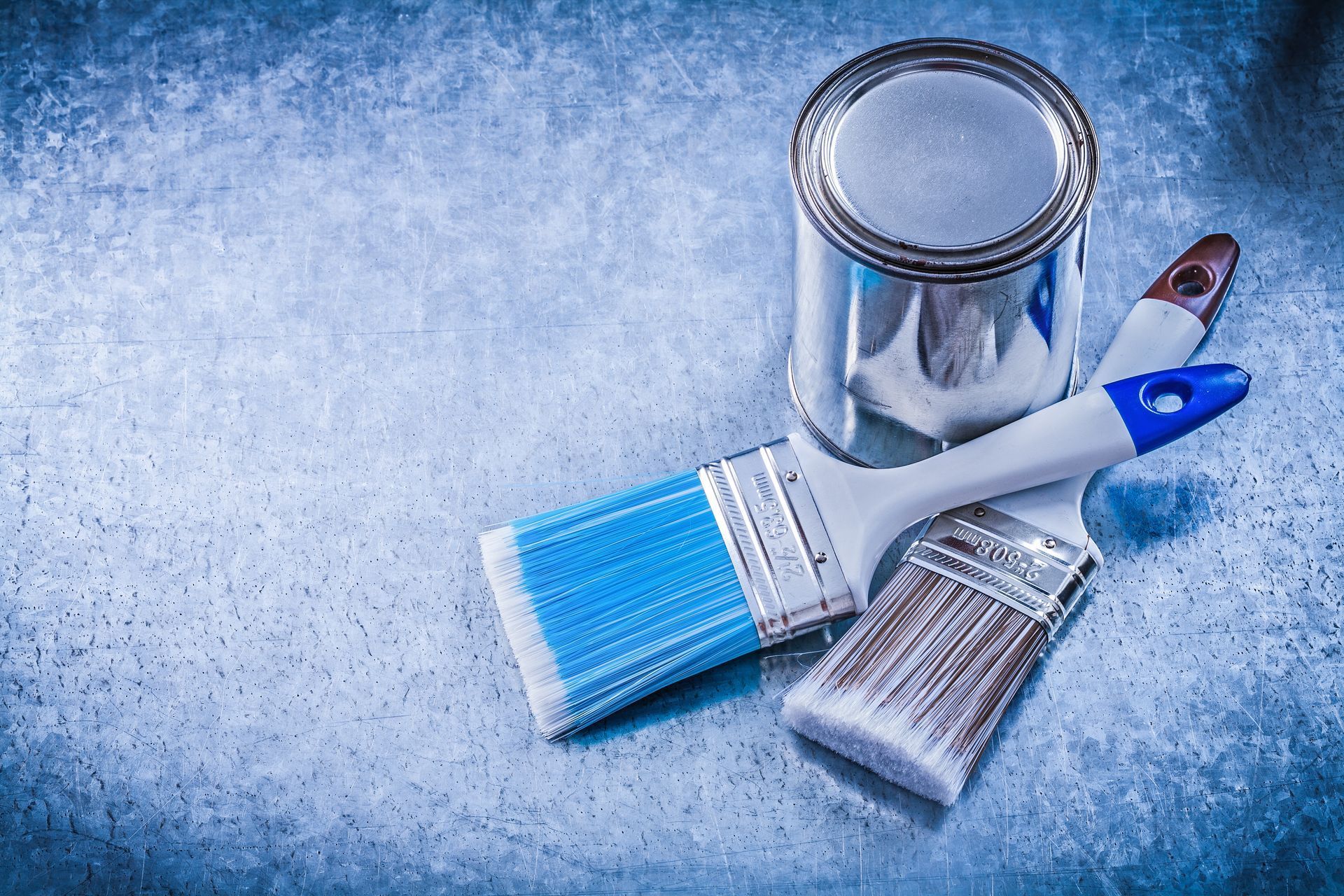 A can of paint and three paint brushes on a blue surface.