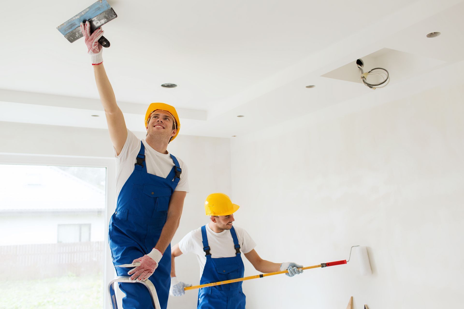 A man is plastering the ceiling while a woman paints the wall.