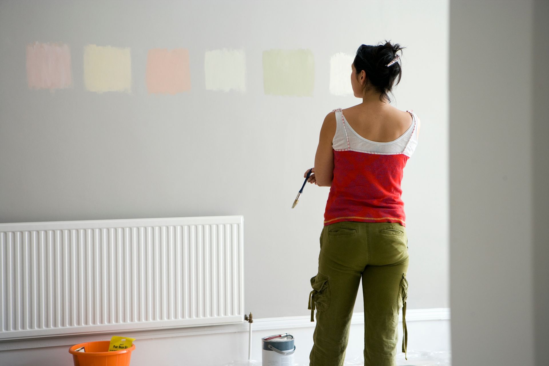 A woman is painting a wall in a room with a brush.