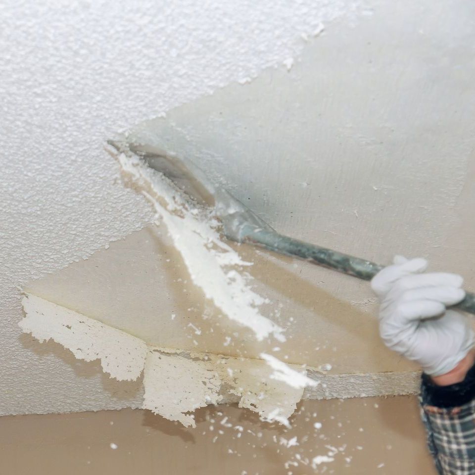 A person is peeling wallpaper from the ceiling with a spatula.