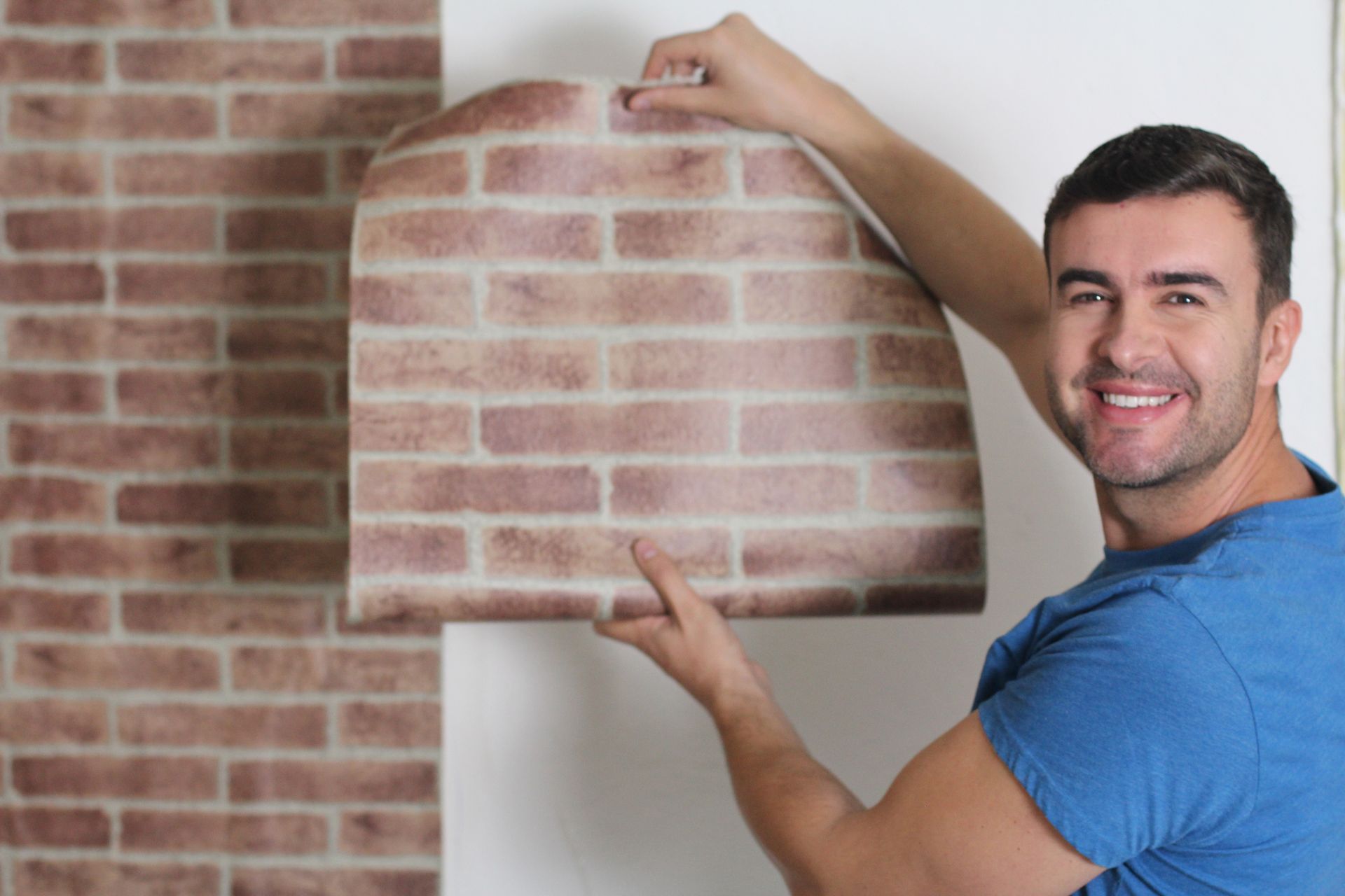 A man is holding a piece of wallpaper that looks like a brick wall.