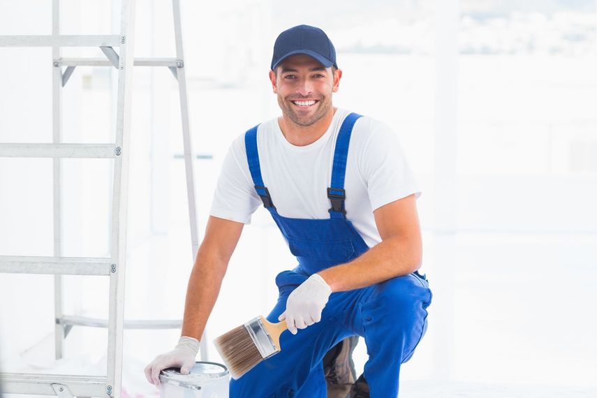 A man is kneeling down holding a paint brush and a bucket of paint.