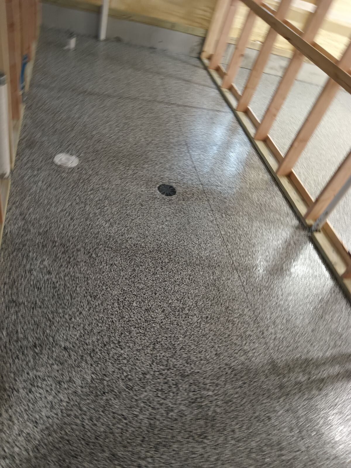 Gray speckled concrete floor with a black drain, next to wooden framing.