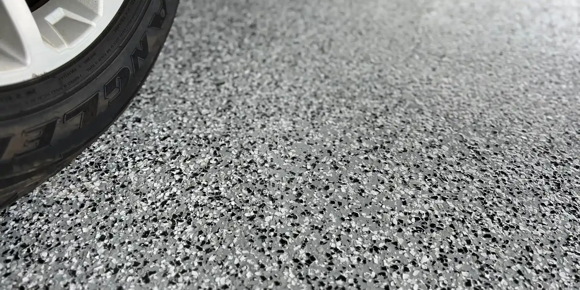 Car tire on speckled, gray garage floor.