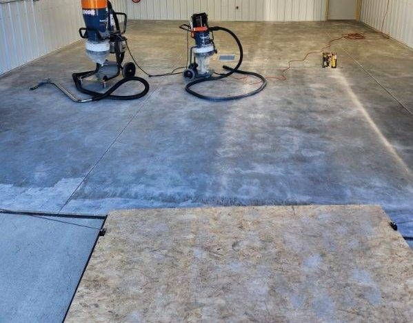 Two vacuum cleaners are sitting on a concrete floor in a garage.