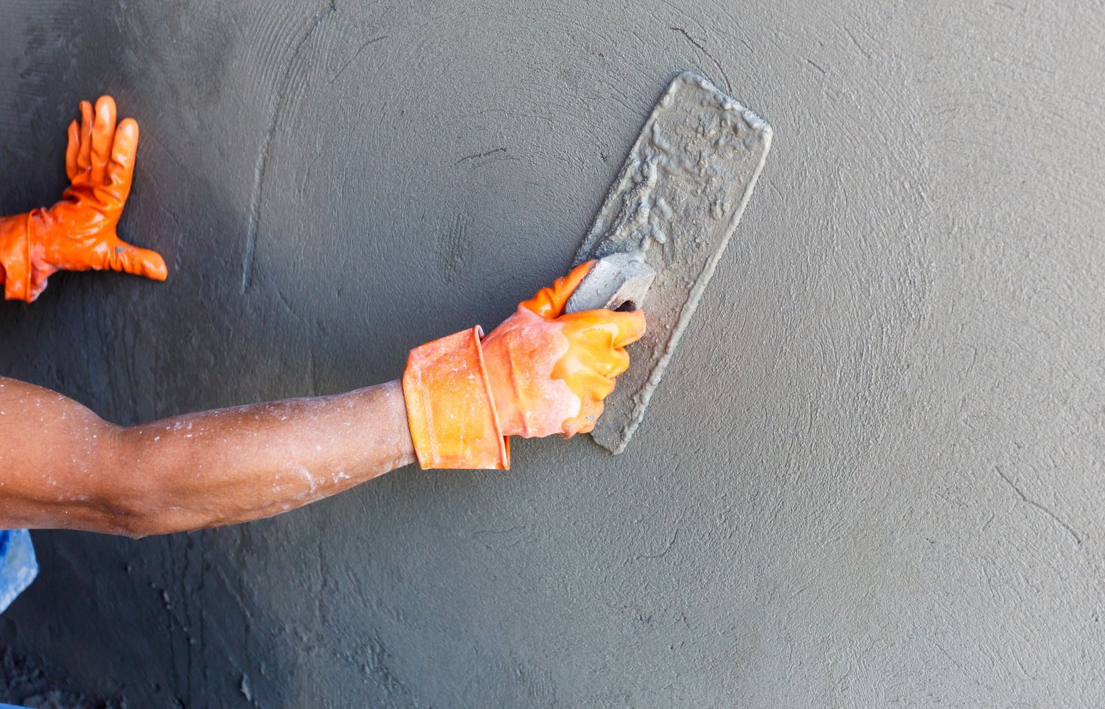 Person applying cement to a wall with a trowel, wearing orange gloves.