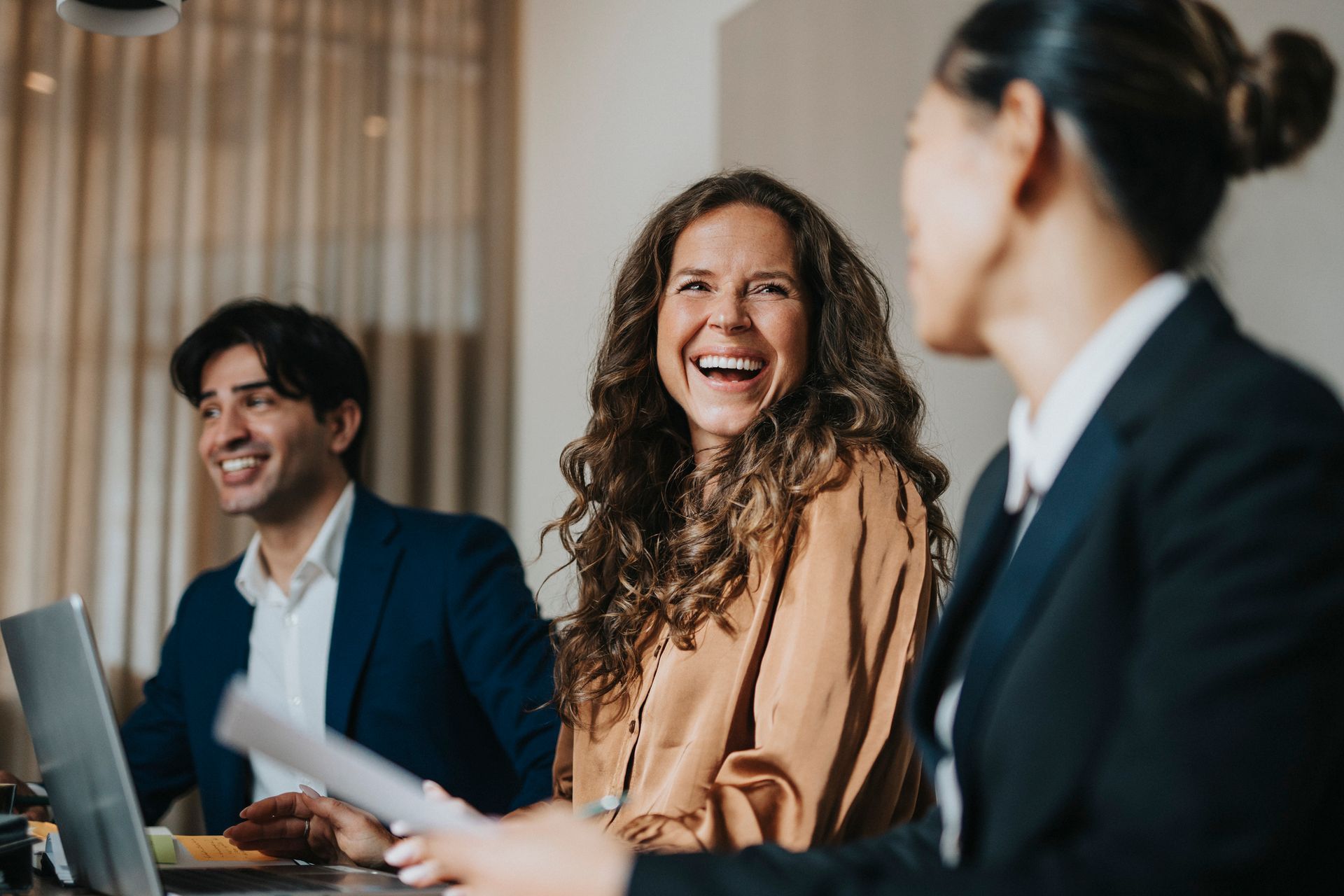 Three people in business attire, laughing in an office.