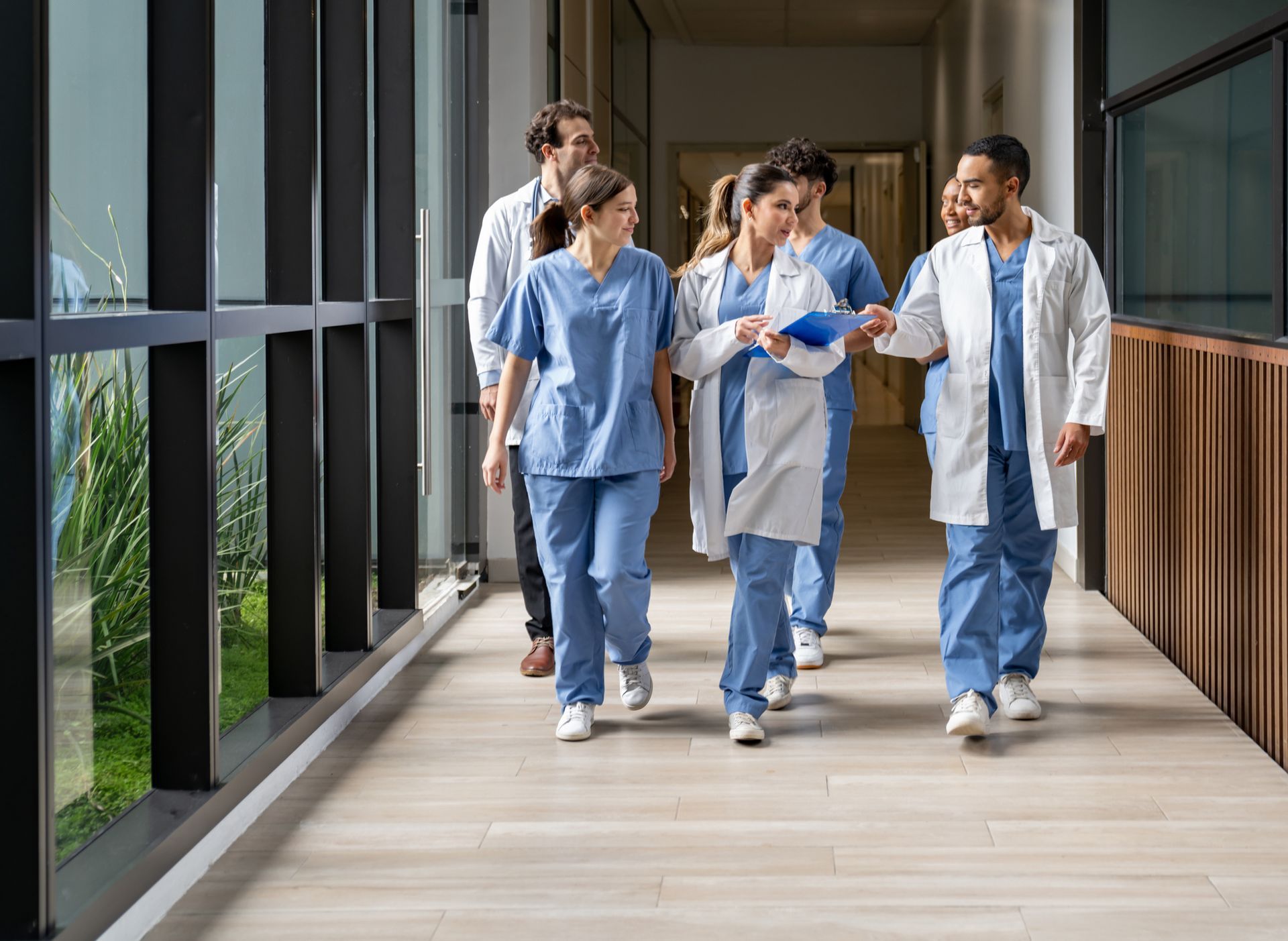 Medical staff walking in a hospital hallway; some wearing scrubs, others in white coats, discussing a patient.