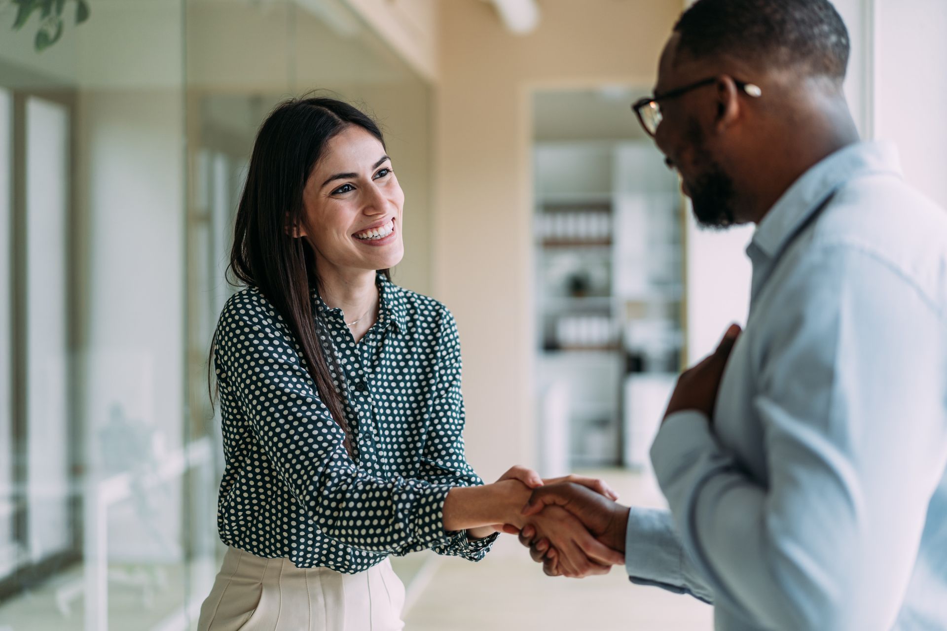 Woman and man in office shaking hands, both smiling.