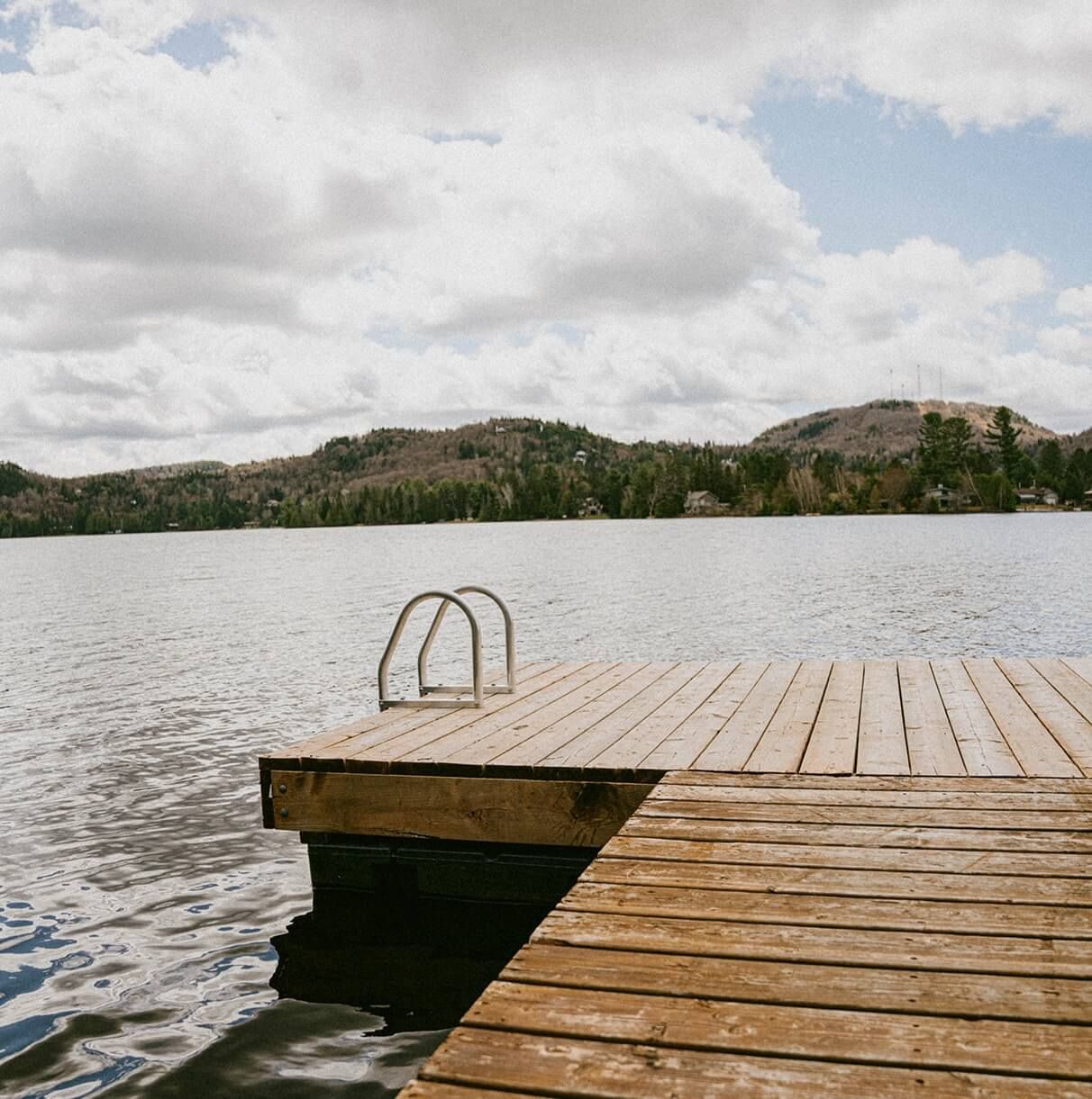 Wooden dock extending into a lake, cloudy sky, hills in background.