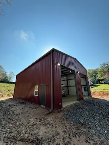 Red metal storage building with open bay doors under a blue sky.