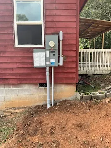 Electrical meter box on red house exterior, with window and porch in background.