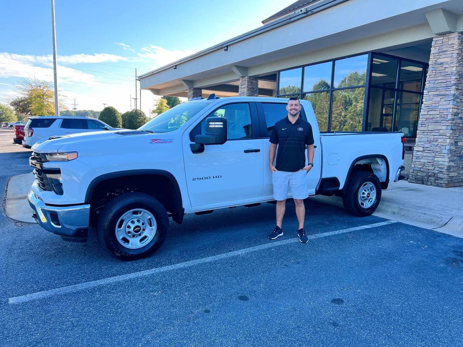 Man standing by a white Chevrolet Silverado pickup truck in a parking lot.