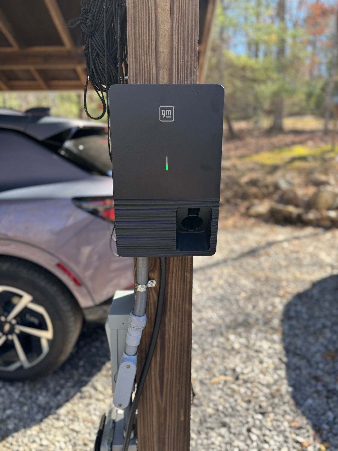 Black electric vehicle charger mounted on a wooden post next to a parked car.