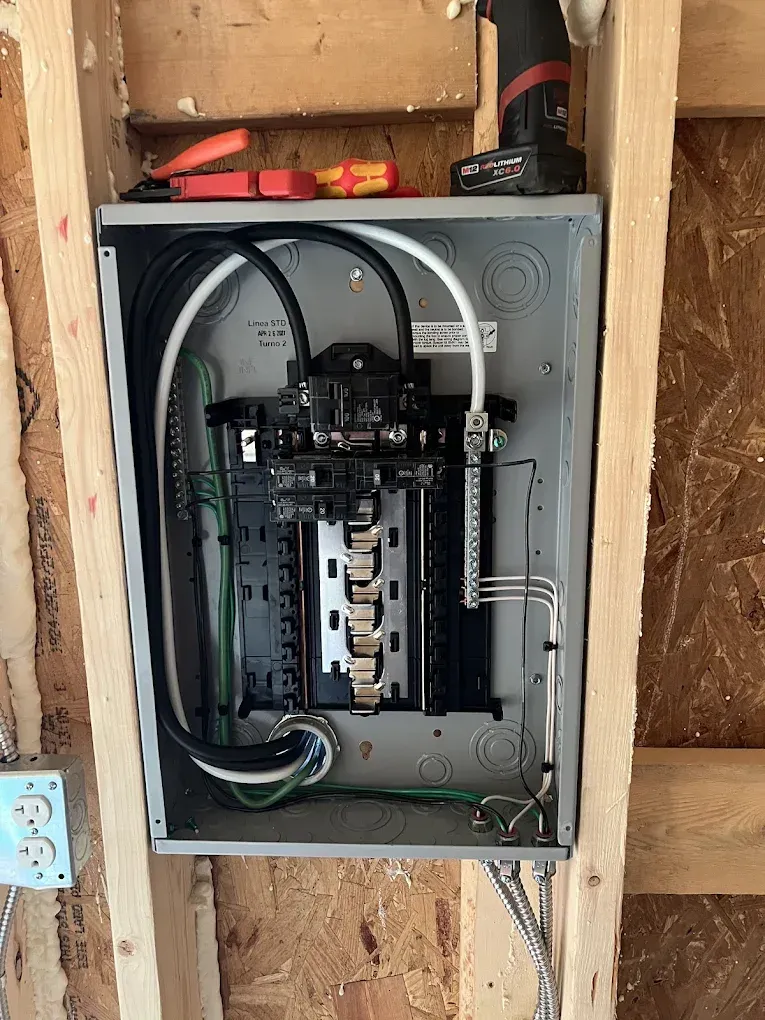 Electrical panel installed in wooden framing; wires and breakers visible.