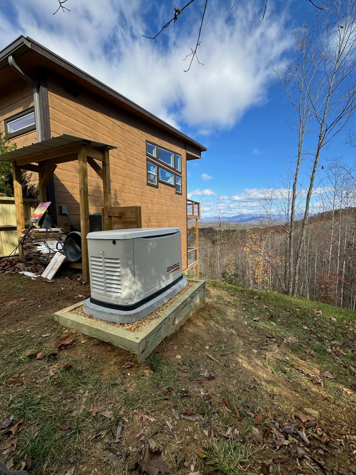Generator on a concrete pad next to a house with mountain view and blue sky.